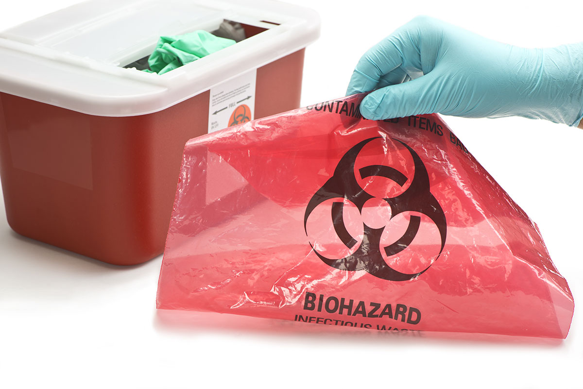 gloved hand holding a red bag of biohazardous waste