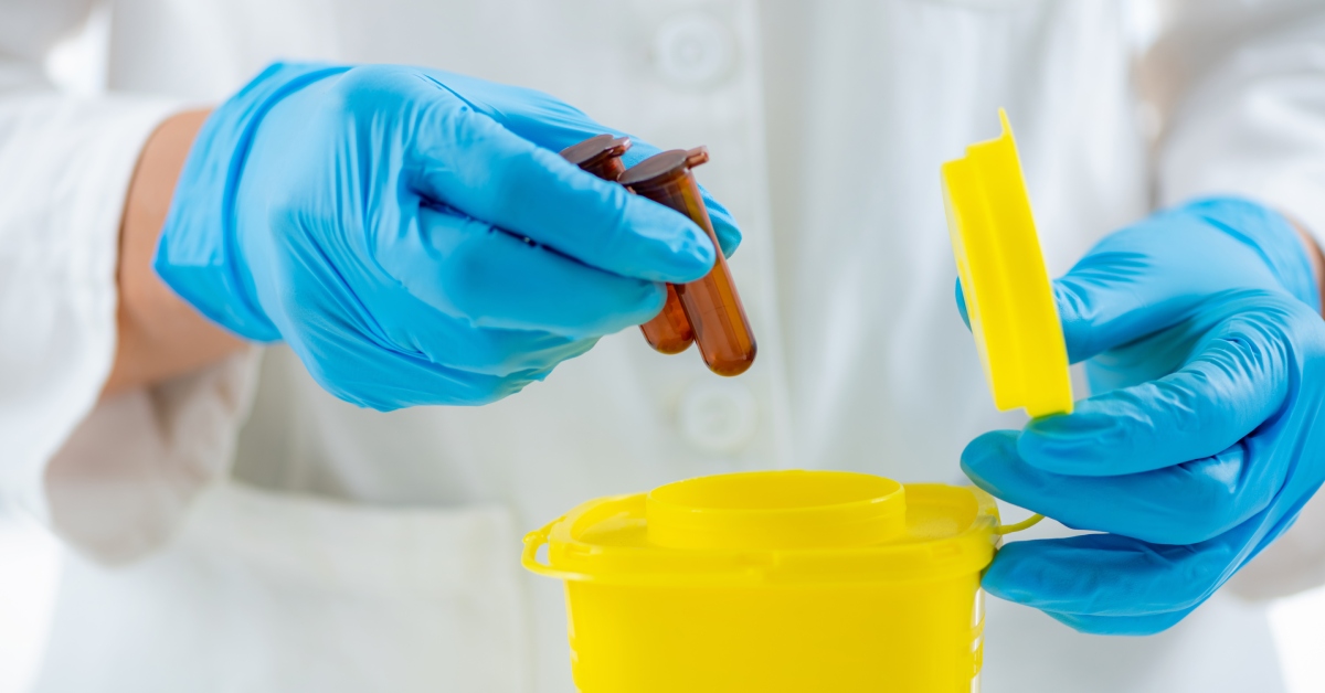 A pair of blue gloved hands are seen in close-up segregating two brown tubes of chemicals in a yellow container.