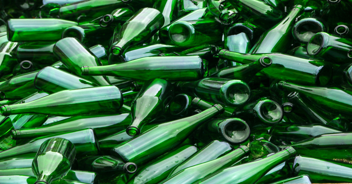 Broken and whole green glass bottles lay on top of each other in a pile that takes up the entirety of the frame.