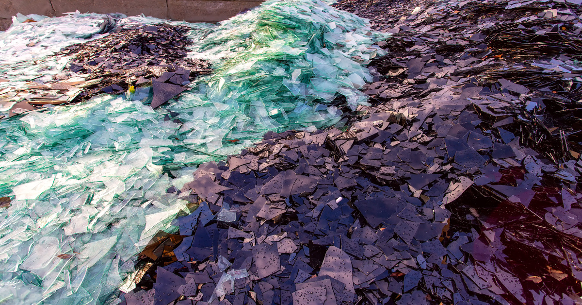Large piles of broken brown, clear, and pale green glass divided by color lined up next to each other outside.