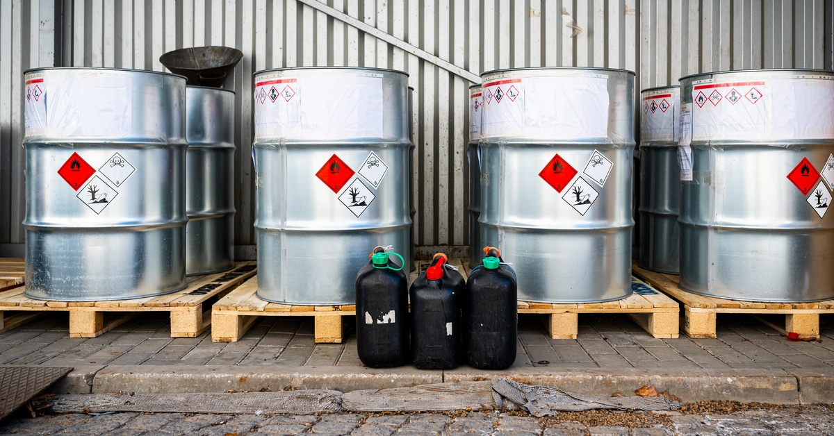 A row of four big silver metal barrels containing hazardous chemicals from laboratories, sitting outside.